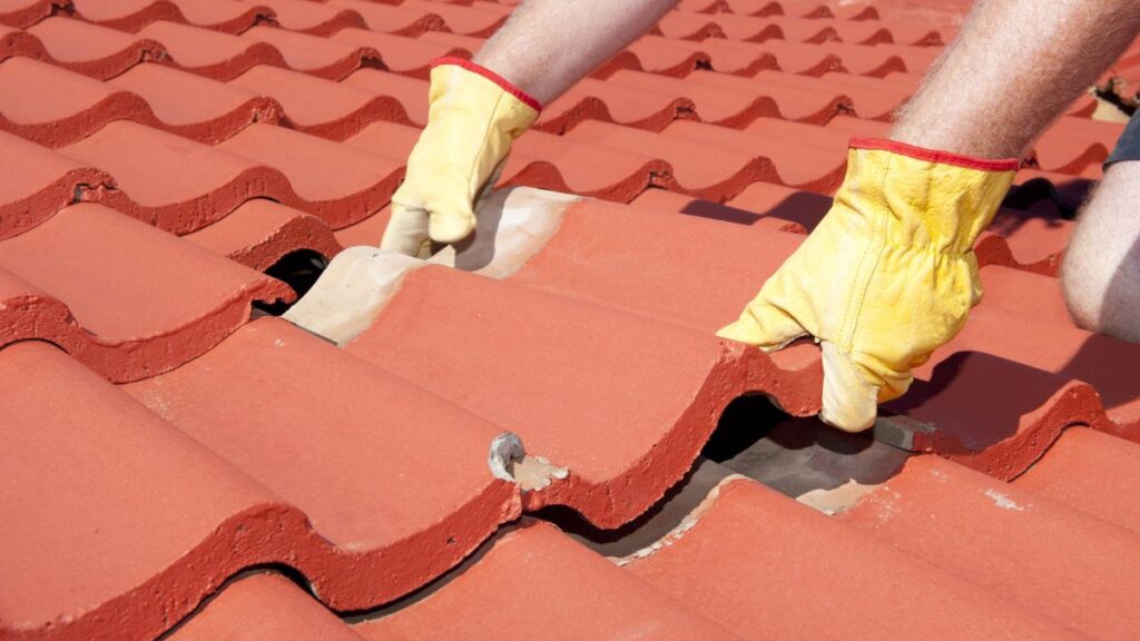 Close-up van betonnen dakpannen die een specialist met gele handschoenen correct plaatst 