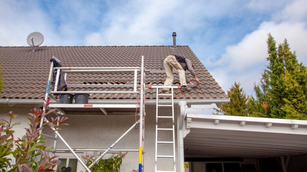 Ervaren dakwerker plaatst met een steiger betonnen dakpannen op een dak 