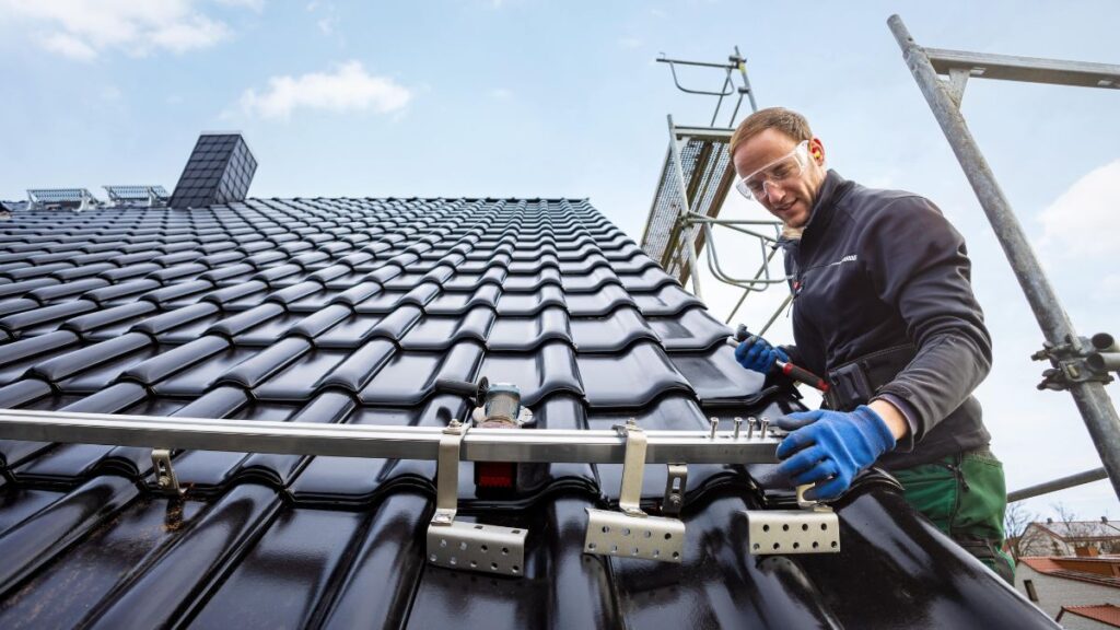 Erkende dakwerker plaatst zonnepaneleninstallatie op een dak met zwarte dakpannen 